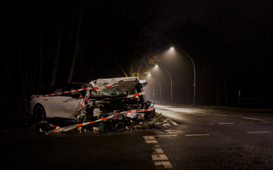 Crashed car surrounded by accident scene tape on a foggy street at night under lamp posts